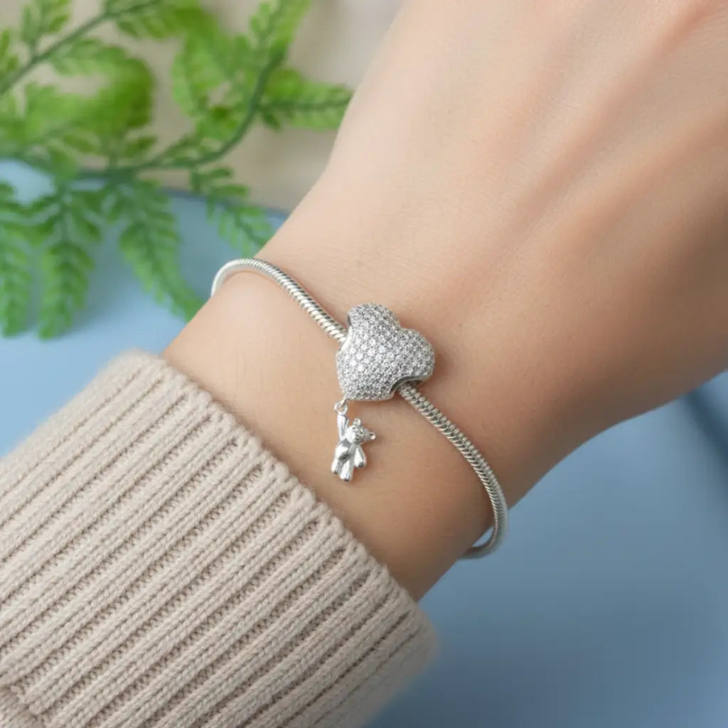 Pulseira prateada com berloque coração cravejado e ursinho em Prata 925, usada no pulso feminino