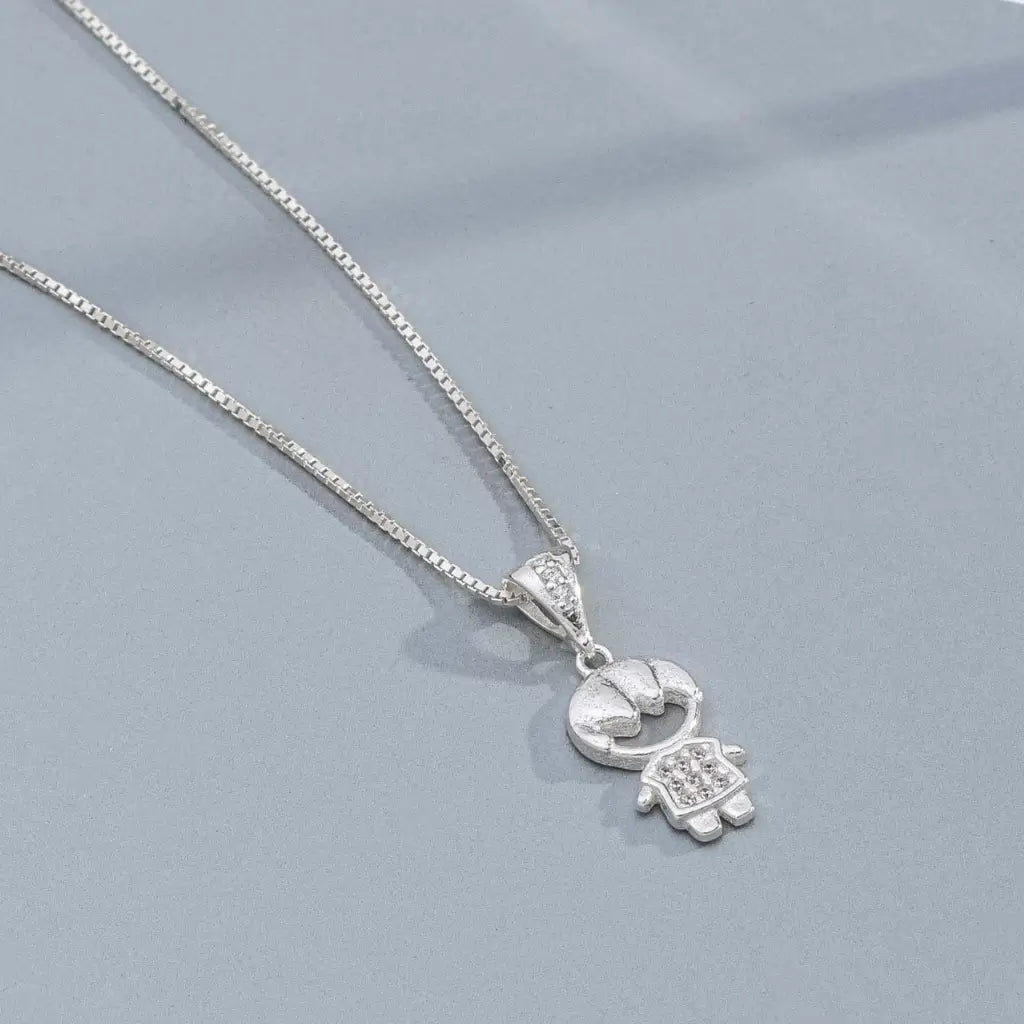 Pingente de menino em prata com detalhes brilhantes, sobre superfície acinzentada moderna.