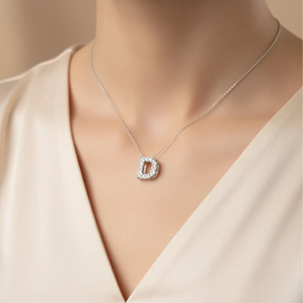 Pingente Letra D em Prata 925 cravejado sendo usado no pescoço com corrente fina e look sofisticado.