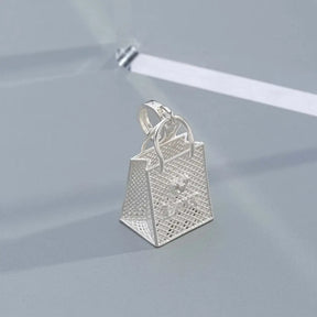 Pingente bolsa prateada com detalhe de strass em forma de coração, acessório romântico.