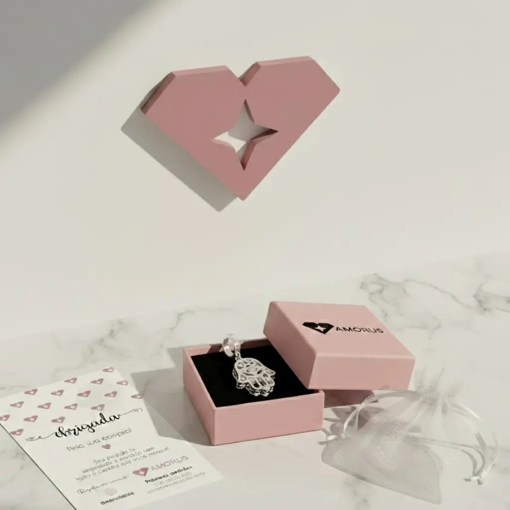 Berloque em Prata 925 Hamsa com detalhes em alto relevo, exibido em caixa rosa da marca AMORUS sobre fundo de mármore branco, acompanhado de cartão de agradecimento.