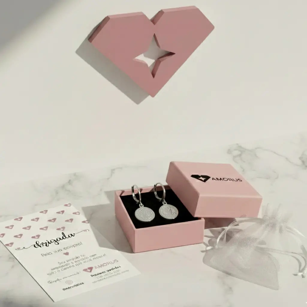 Brincos de argola São Bento em embalagem rosa da AMORUS, com cartão e saquinho ao lado.