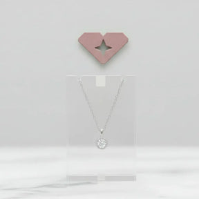 Colar feminino ponto de luz em prata 925 exposto em suporte acrílico, com fundo neutro e decoração minimalista 